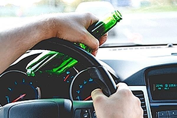 На зображенні водій тримає пляшку алкоголю за кермом автомобіля.